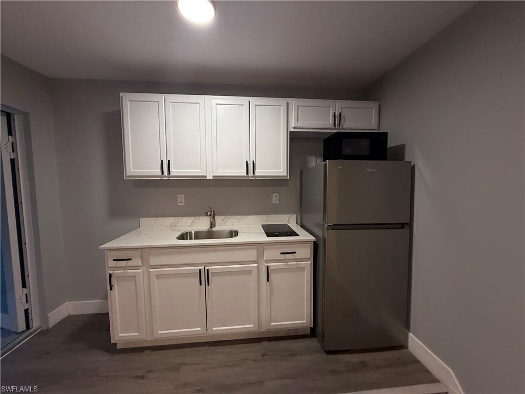 Kitchen featuring freestanding refrigerator, white cabinetry, light stone counters, and dark wood-type flooring