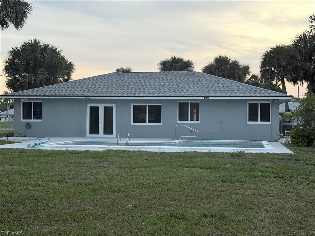 Back of property at dusk with french doors, stucco siding, and a yard