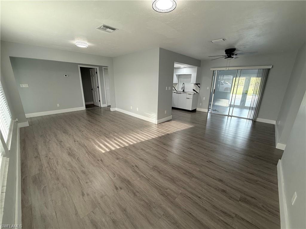 Unfurnished living room featuring a ceiling fan and dark wood-style floors