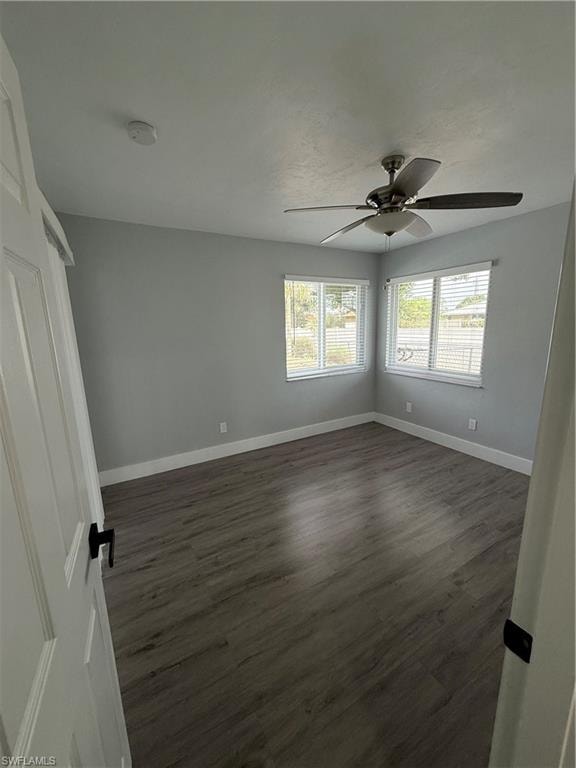 Empty room with a smoke detector, ceiling fan, and dark wood-style floors