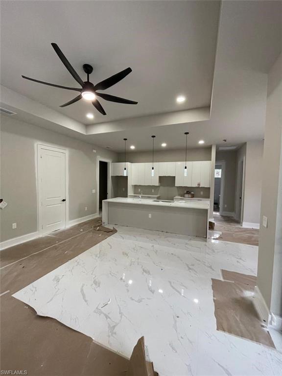 Unfurnished living room featuring a tray ceiling, recessed lighting, and a ceiling fan