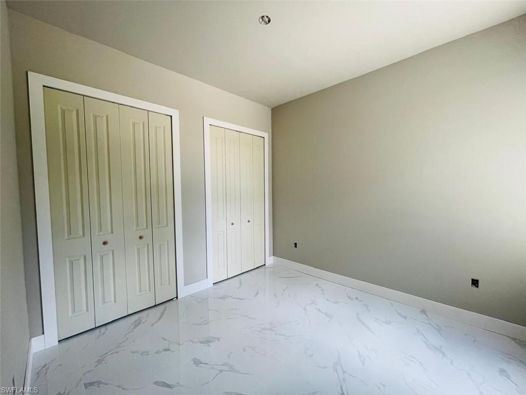 Unfurnished bedroom with multiple closets, light marble finish flooring, and baseboards