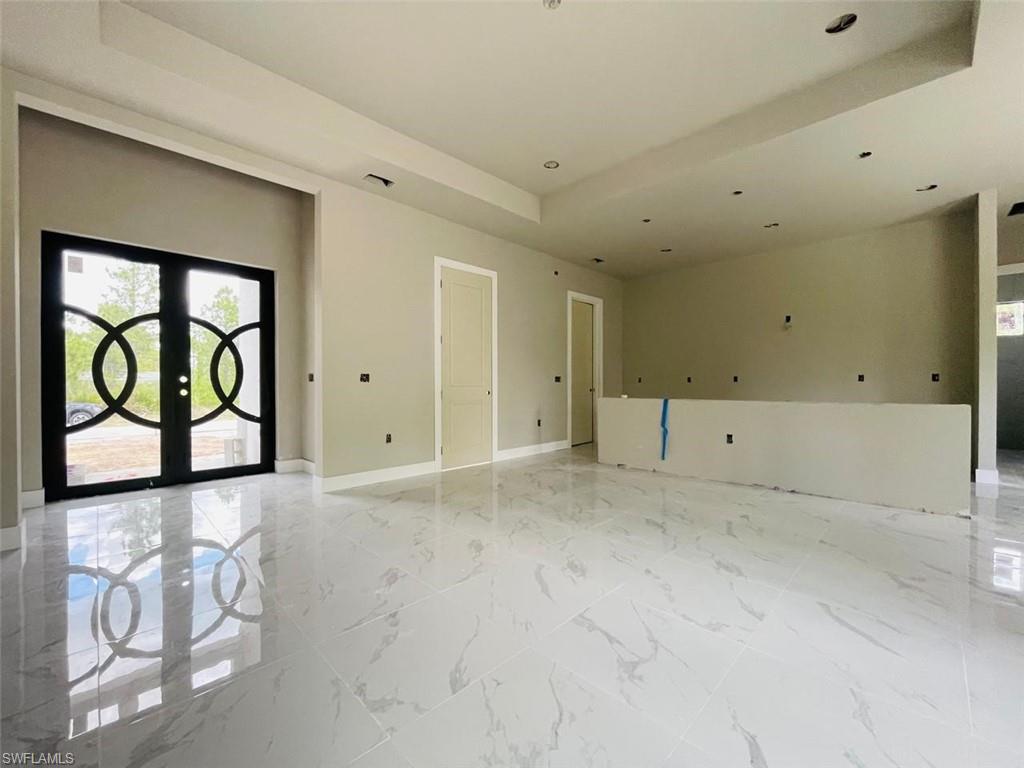 Empty room with a tray ceiling, french doors, baseboards, recessed lighting, and light marble finish floors