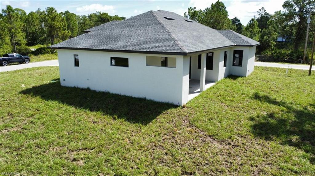 Rear view of property featuring a lawn, stucco siding, roof with shingles, and a patio