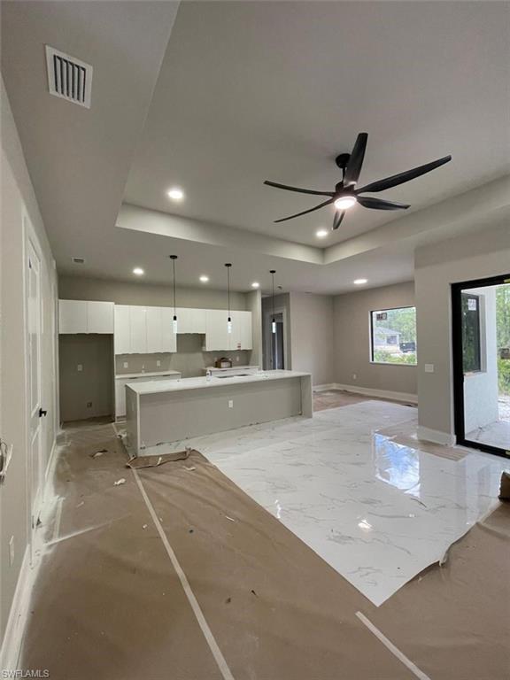 Unfurnished living room with a tray ceiling, ceiling fan, recessed lighting, and marble tiled floors