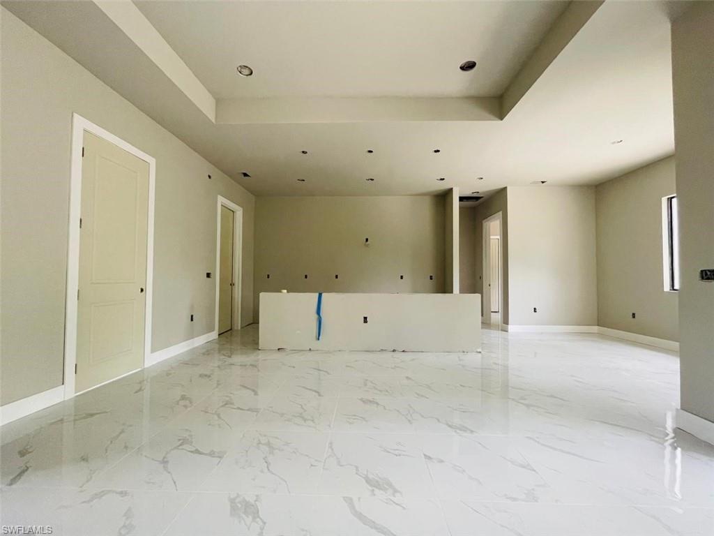 Empty room featuring a tray ceiling, light marble finish flooring, baseboards, and recessed lighting