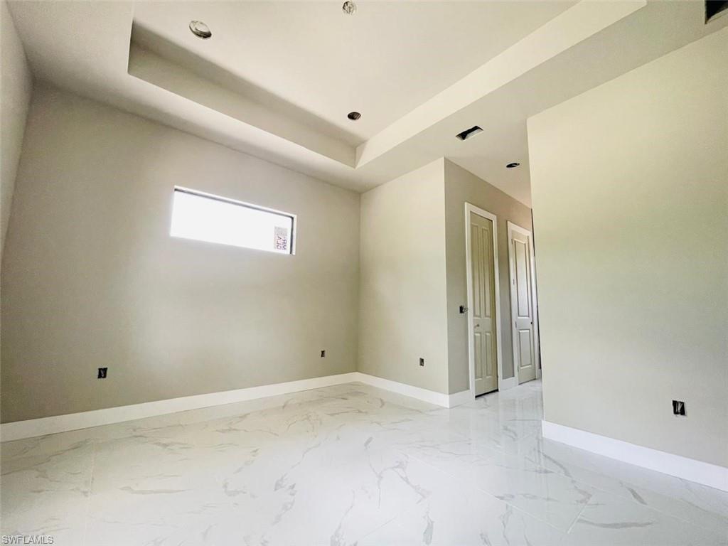 Empty room featuring baseboards, light marble finish flooring, a tray ceiling, and recessed lighting