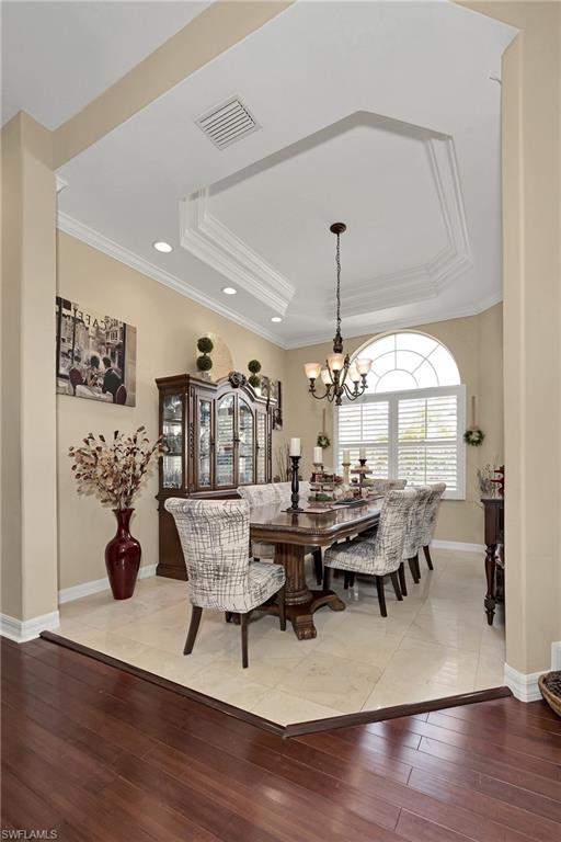 Dining room featuring light wood-type flooring, a raised ceiling, a chandelier, recessed lighting, and crown molding