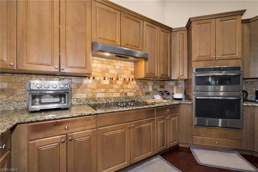 Kitchen featuring under cabinet range hood, double oven, black electric cooktop, and light stone counters