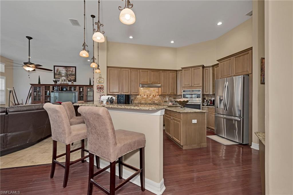 Kitchen with stainless steel appliances, under cabinet range hood, backsplash, open floor plan, and dark wood-type flooring