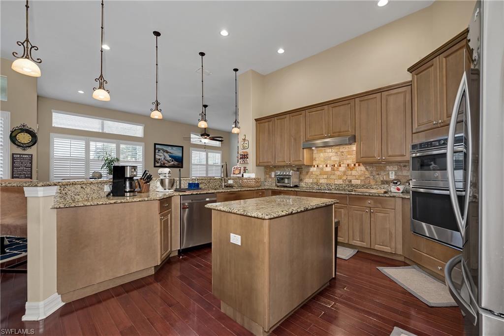 Kitchen featuring appliances with stainless steel finishes, a peninsula, a center island, backsplash, and dark wood finished floors