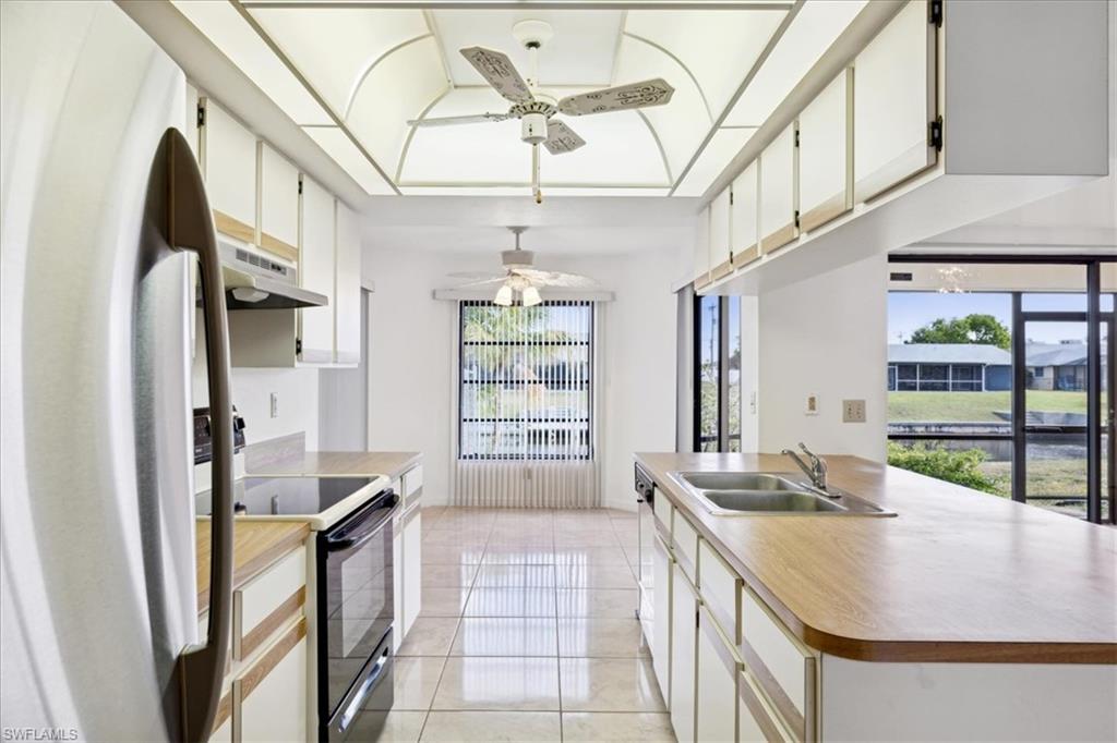 Kitchen featuring freestanding refrigerator, a sink, ceiling fan, black electric range oven, and under cabinet range hood