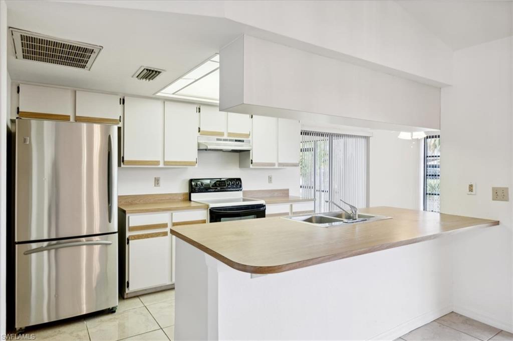 Kitchen featuring freestanding refrigerator, range with electric cooktop, a sink, under cabinet range hood, and light tile patterned floors