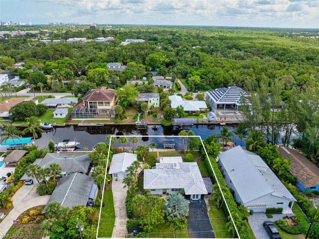 Aerial perspective of suburban area with property parcel outlined, a nearby body of water, and a heavily wooded area