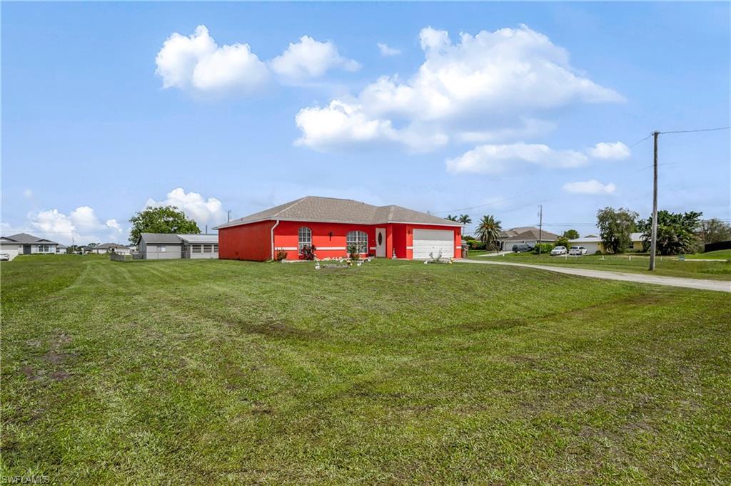 View of grassy yard featuring a garage and driveway