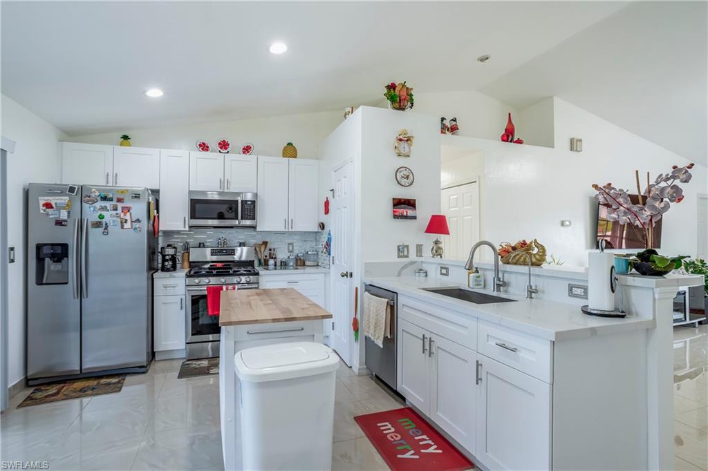 Kitchen featuring appliances with stainless steel finishes, lofted ceiling, butcher block counters, a sink, and a kitchen island