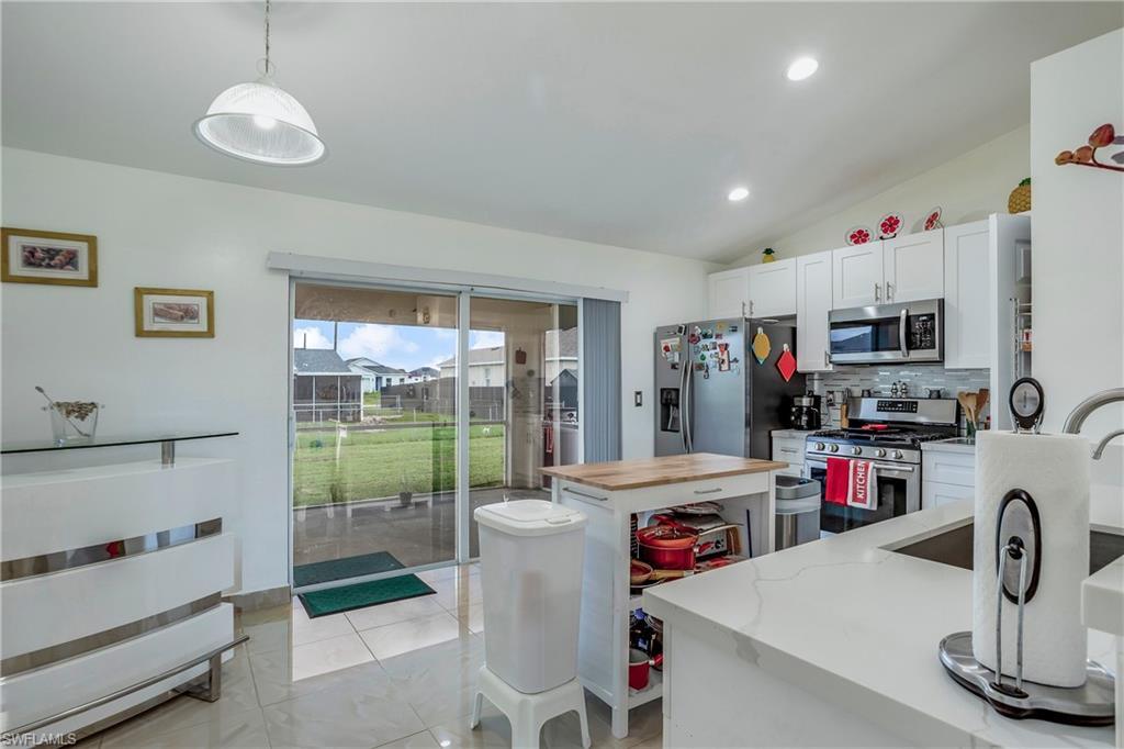 Kitchen with appliances with stainless steel finishes, vaulted ceiling, backsplash, pendant lighting, and light stone counters