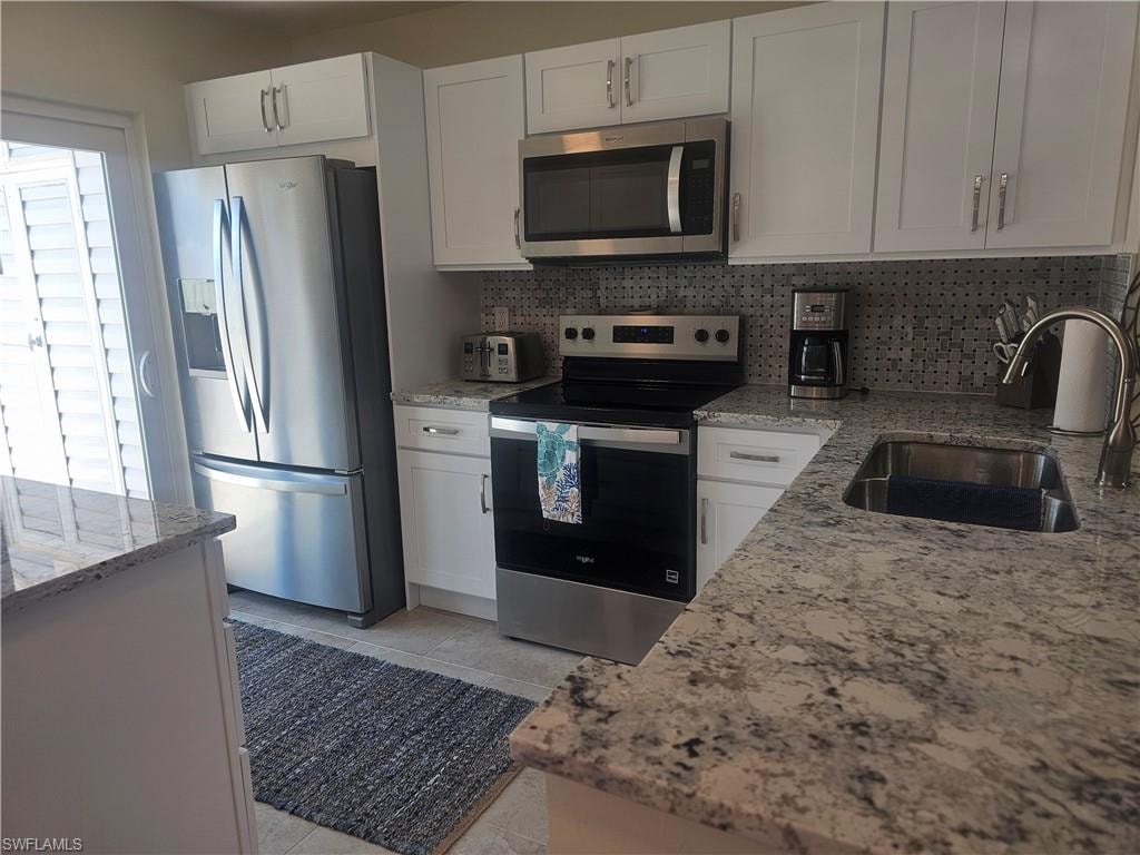 Kitchen with appliances with stainless steel finishes, white cabinets, light stone countertops, and decorative backsplash