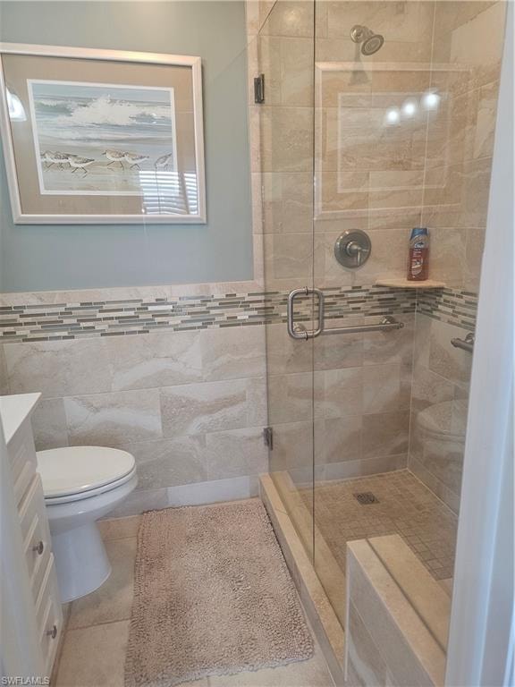 Bathroom featuring a stall shower, vanity, tile patterned flooring, tile walls, and a wainscoted wall