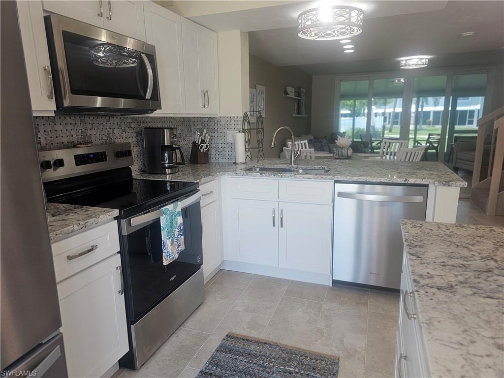 Kitchen featuring stainless steel appliances, backsplash, a peninsula, white cabinets, and light stone counters