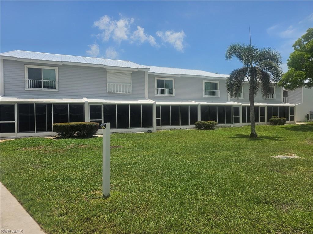 Rear view of property featuring a sunroom, a yard, and a metal roof