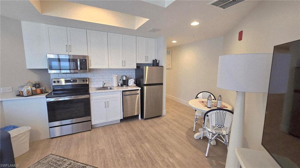 Kitchen featuring appliances with stainless steel finishes, decorative backsplash, white cabinets, light countertops, and light wood-style flooring