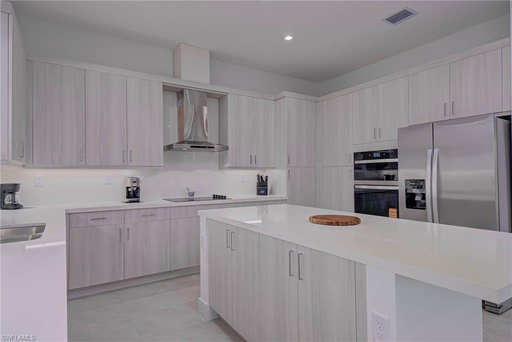 Kitchen with wall chimney range hood, appliances with stainless steel finishes, modern cabinets, light countertops, and a center island