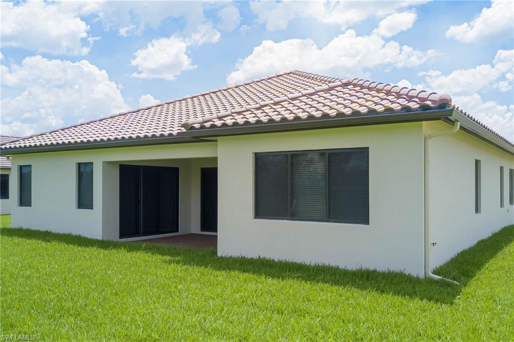 Back of property with stucco siding, a tiled roof, and a lawn