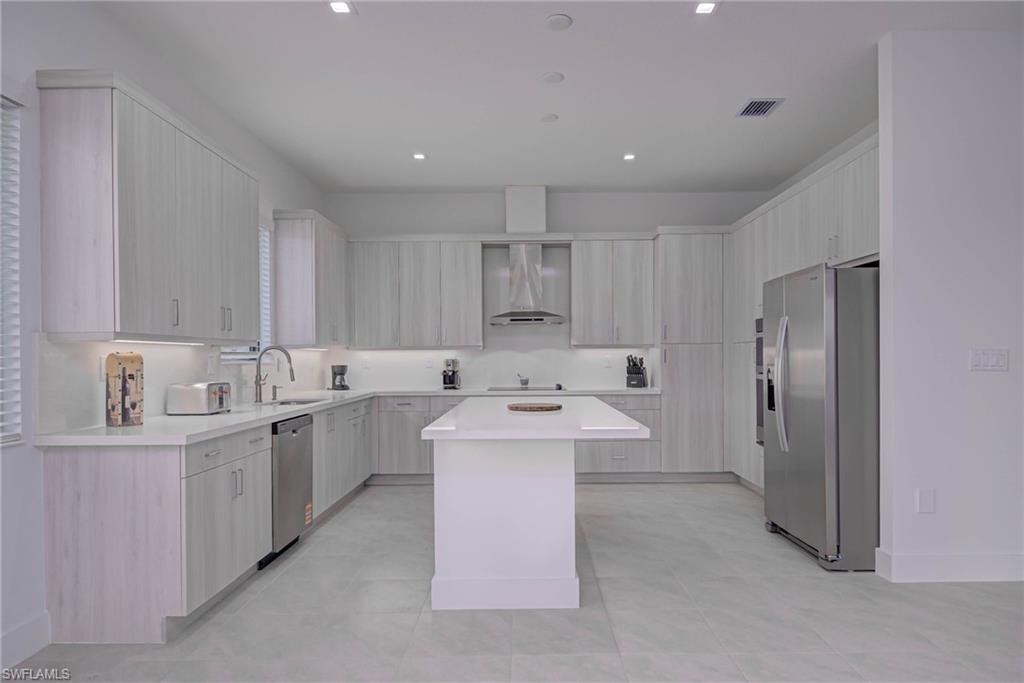 Kitchen with stainless steel appliances, wall chimney exhaust hood, a kitchen island, modern cabinets, and recessed lighting