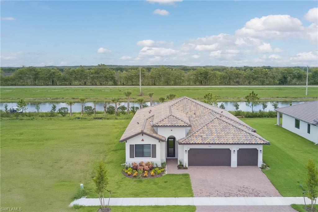 View of front facade featuring an attached garage, a water view, stucco siding, decorative driveway, and a front lawn