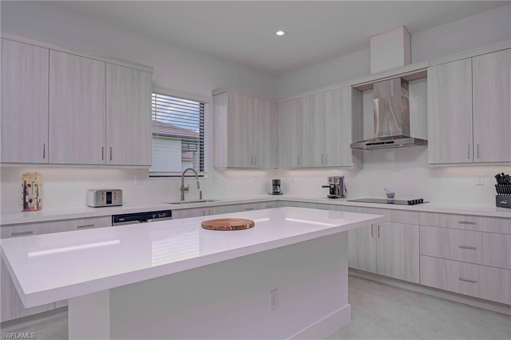 Kitchen with wall chimney exhaust hood, light countertops, modern cabinets, stainless steel dishwasher, and a kitchen island