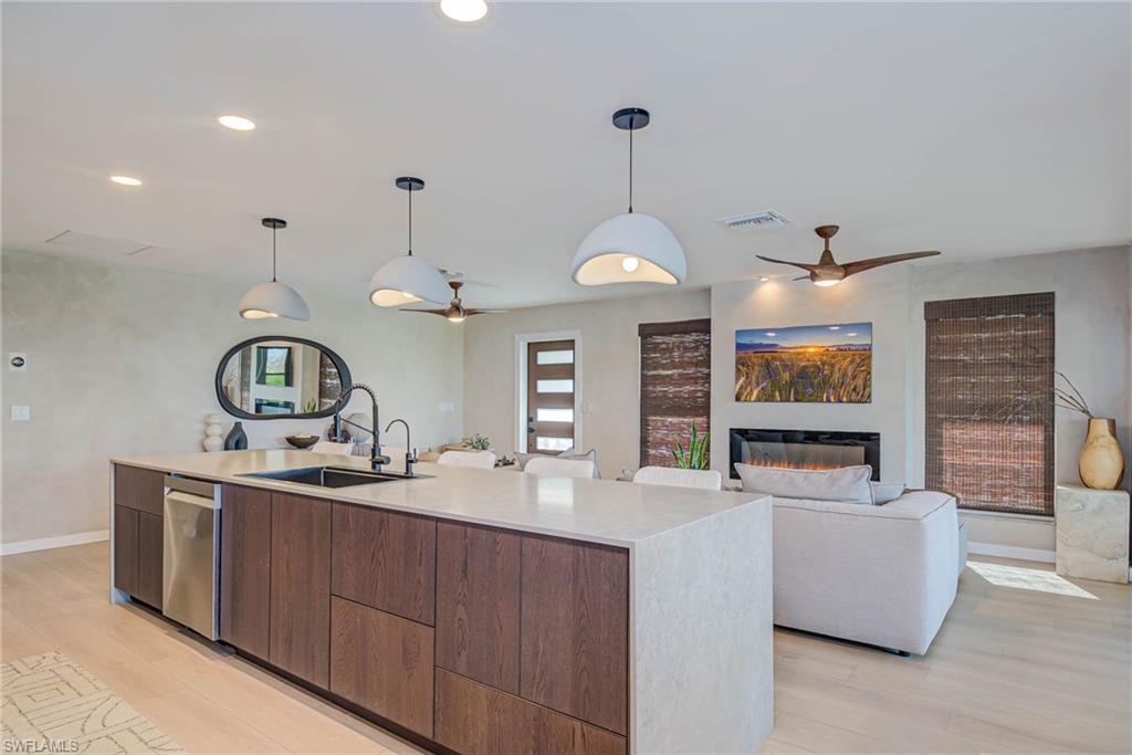 NEW front door, gas fireplace, NEW impact windows , Kitchen with ceiling fan, stainless steel dishwasher, light wood-style flooring, a center island with sink, and recessed lighting