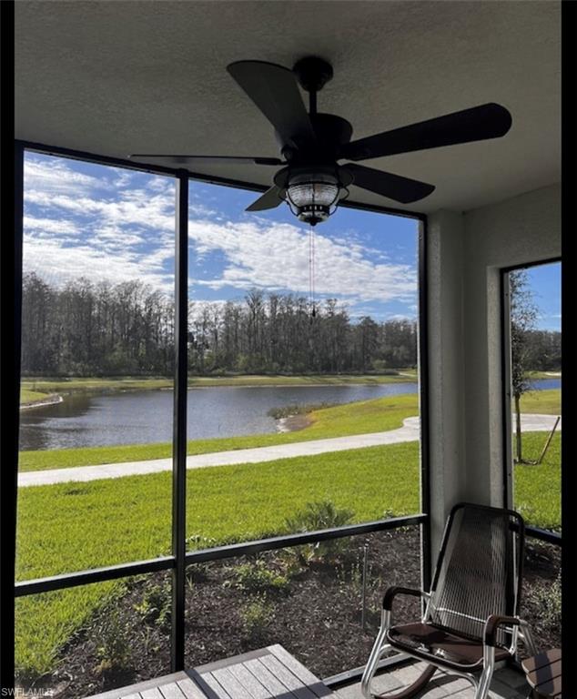Sunroom featuring a water view, view of scattered trees, and a ceiling fan