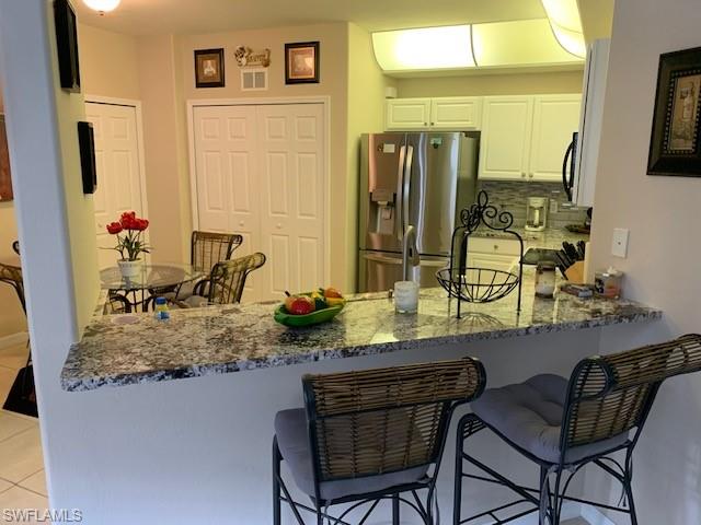 Kitchen with stainless steel refrigerator with ice dispenser, a peninsula, dark stone counters, white cabinets, and light tile patterned floors