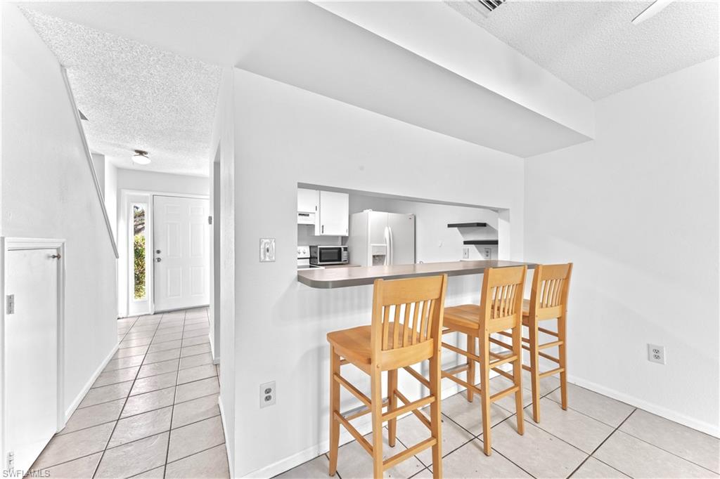 Kitchen with white cabinets, a kitchen breakfast bar, a textured ceiling, and white fridge with ice dispenser