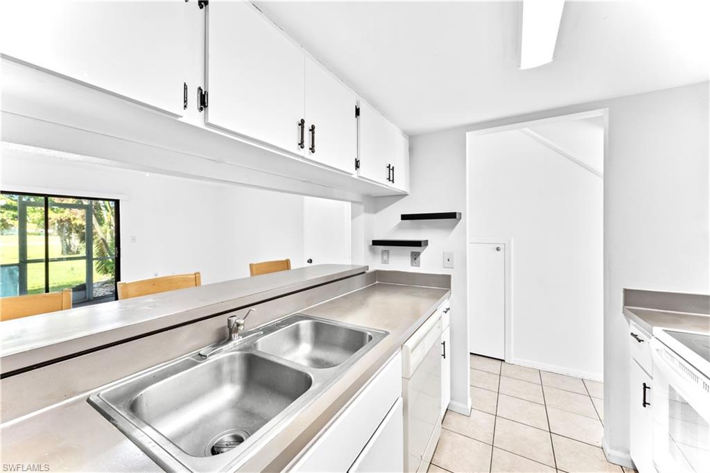 Kitchen with stainless steel counters, white cabinetry, light tile patterned floors, sink, and white appliances