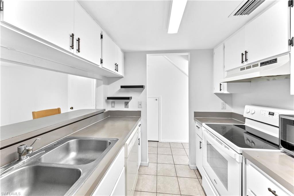 Kitchen with white cabinetry, sink, white appliances, and light tile patterned floors