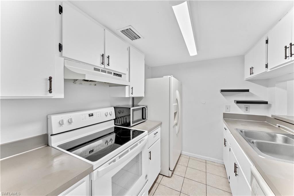 Kitchen with white cabinets, white appliances, light tile patterned floors, and sink