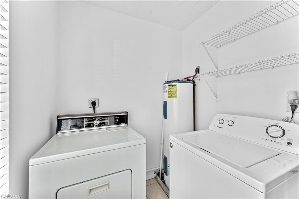 Clothes washing area featuring electric water heater, light tile patterned floors, and washer and dryer