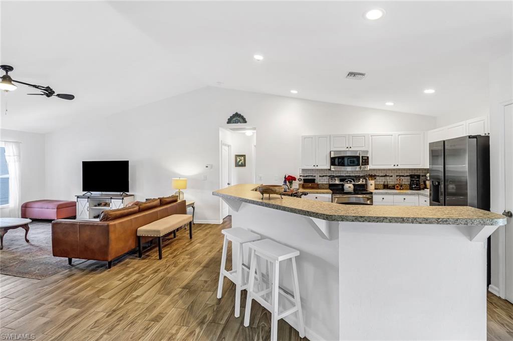 Kitchen featuring stainless steel appliances, lofted ceiling, a breakfast bar, light wood-style floors, and white cabinets