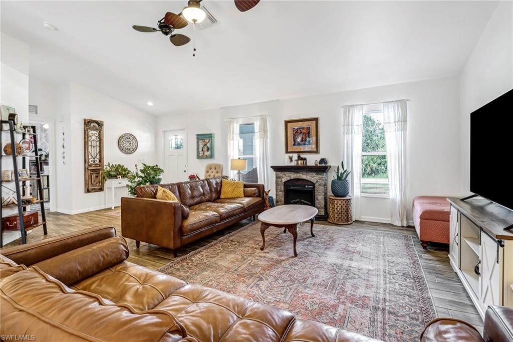 Living room featuring ceiling fan, wood finished floors, a stone fireplace, lofted ceiling, and recessed lighting