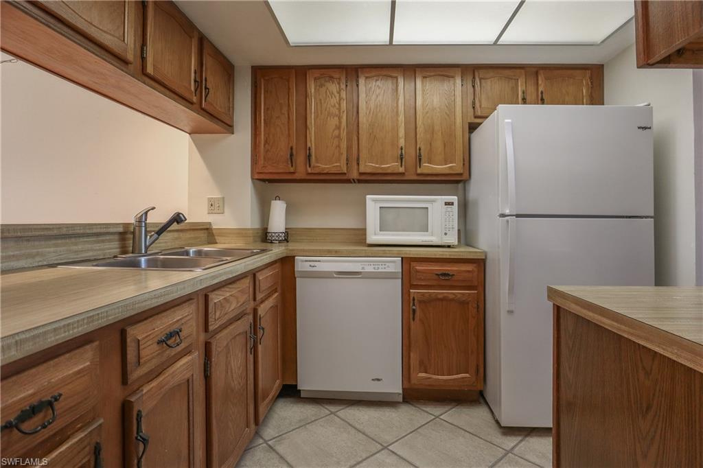 Kitchen featuring brown cabinets, white appliances, light countertops, and light tile patterned flooring