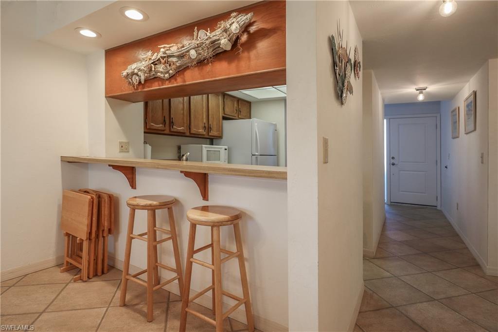 Kitchen featuring light tile patterned floors, a breakfast bar, white appliances, light countertops, and recessed lighting