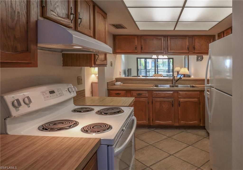 Kitchen with white appliances, under cabinet range hood, light tile patterned flooring, and brown cabinetry