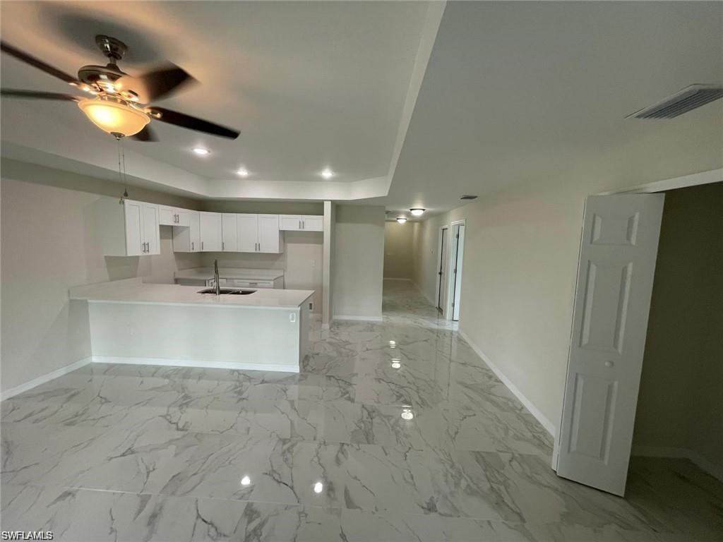 Kitchen featuring a peninsula, a raised ceiling, ceiling fan, white cabinets, and light countertops