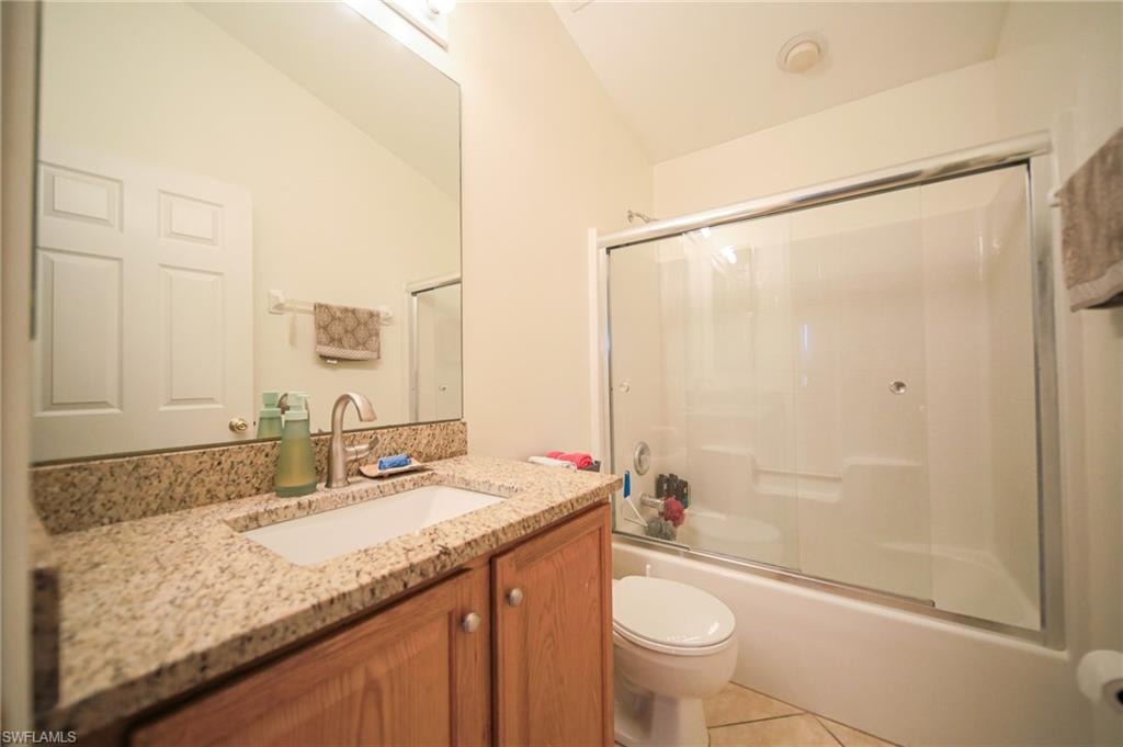 Full bath with tile patterned flooring, vanity, enclosed tub / shower combo, and vaulted ceiling