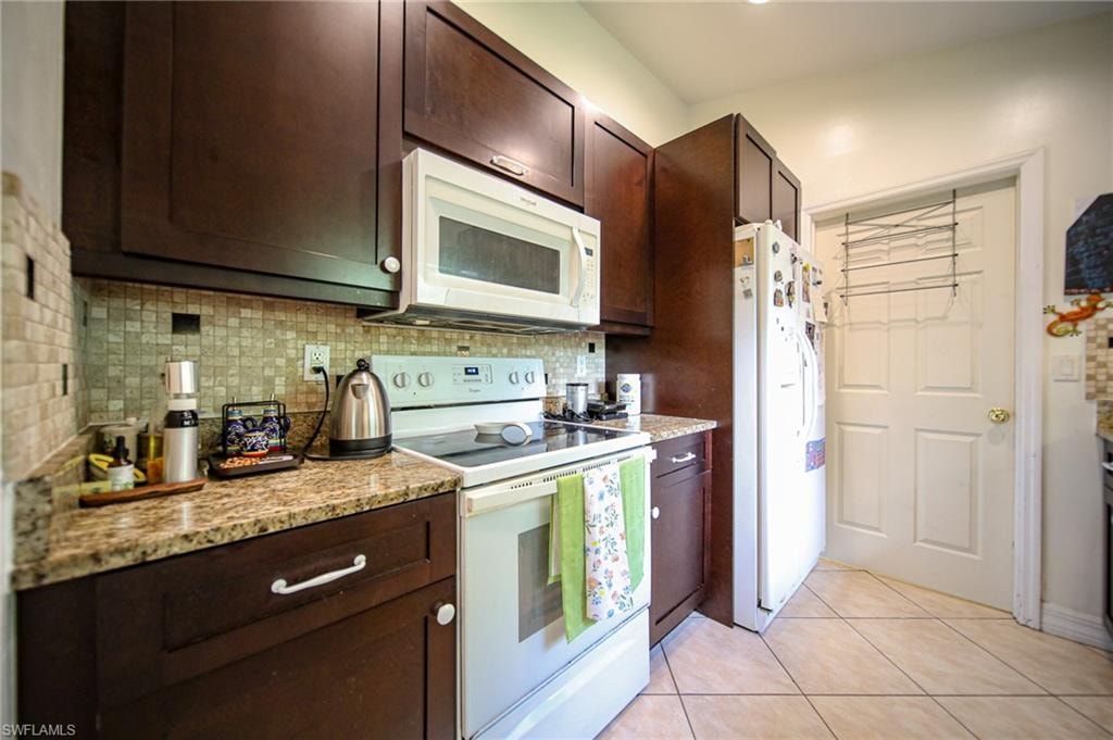 Kitchen featuring white appliances, backsplash, and dark brown cabinetry