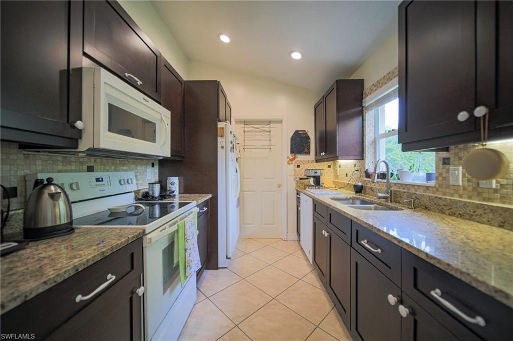 Kitchen featuring white appliances, vaulted ceiling, decorative backsplash, light stone counters, and light tile patterned floors