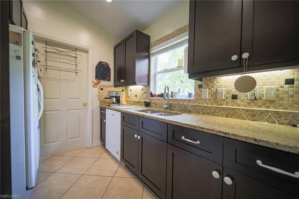 Kitchen featuring white appliances, tasteful backsplash, light tile patterned floors, and light stone countertops