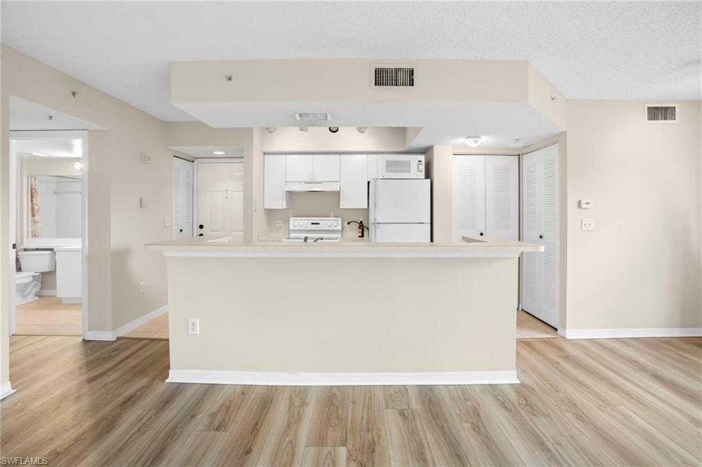 Kitchen with white appliances, under cabinet range hood, light wood-type flooring, white cabinets, and light countertops